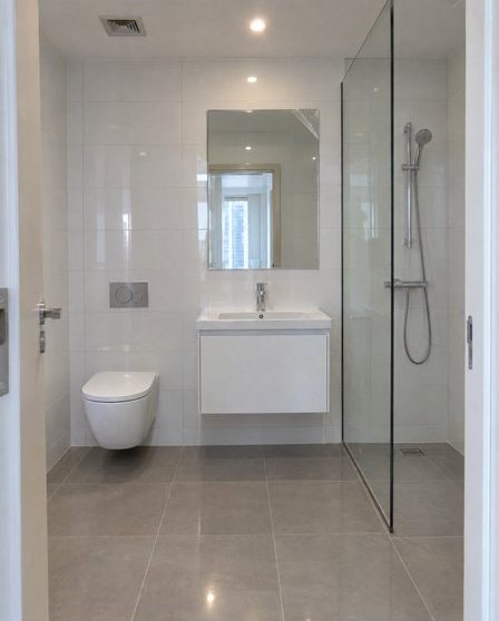 The bathroom at handover: white tiles, a wall-hung basin and a glass shower screen