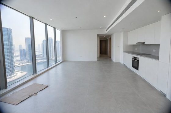 The living room at handover: empty and all white, with floor-to-ceiling windows and a white kitchen along the wall