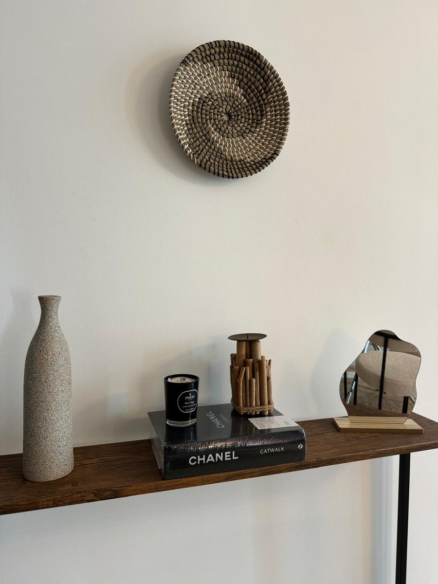 Styled console: a woven wall plate, a textured vase, books and a small sculptural mirror