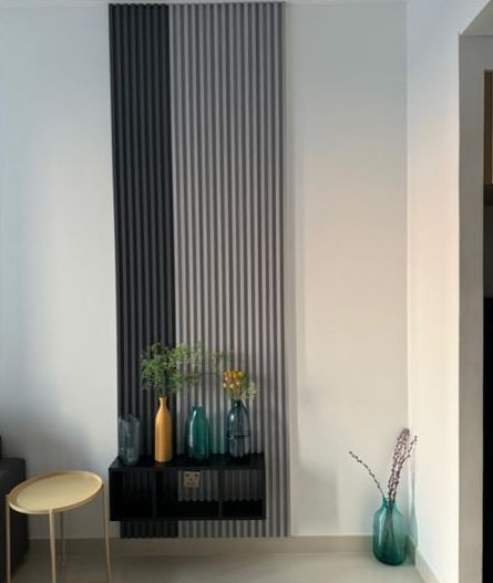 The slatted wall corner before, with coloured glass vases and a yellow side table