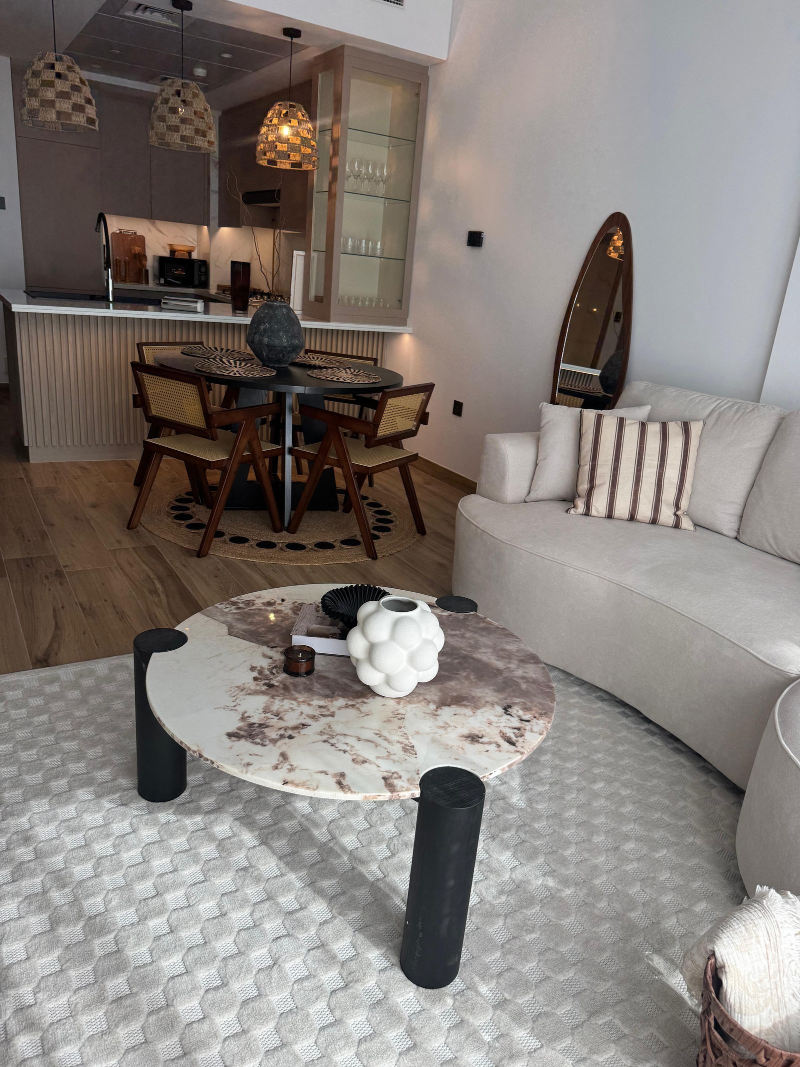 The living area of the JVC apartment: a curved sofa and marble-topped coffee table, with the dining table and kitchen behind
