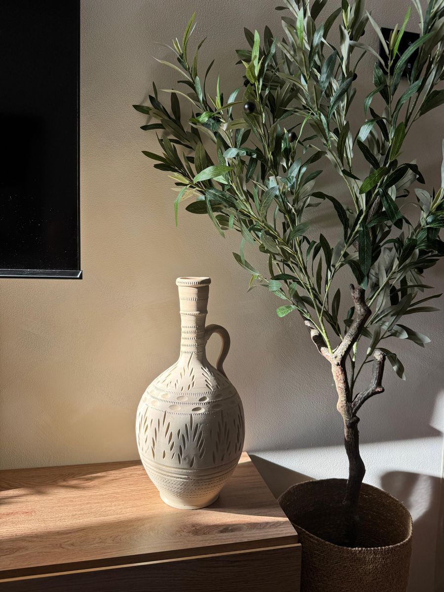 A carved ceramic jug beside an olive tree