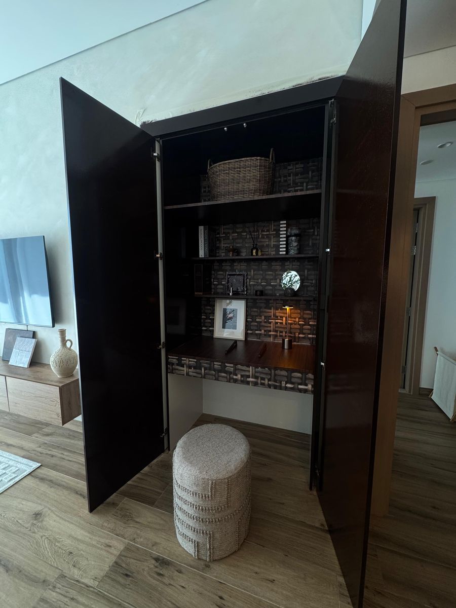 Tall dark-wood cabinet opened to reveal a desk and a woven pouf
