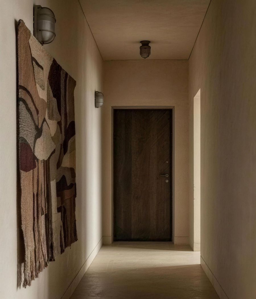 The hallway after: limewash walls, a dark wood front door and a large woven wall hanging