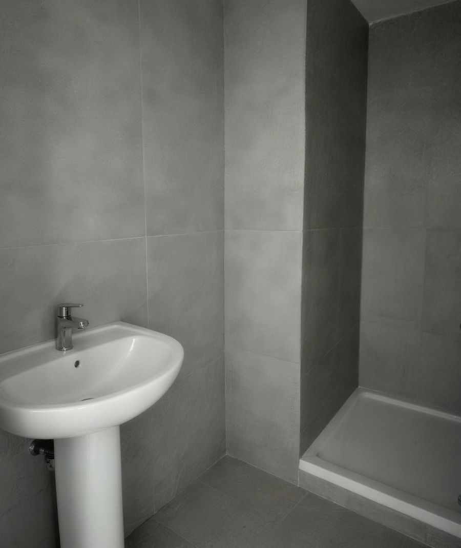 The bathroom at handover: grey tiles, a pedestal basin and a shower tray