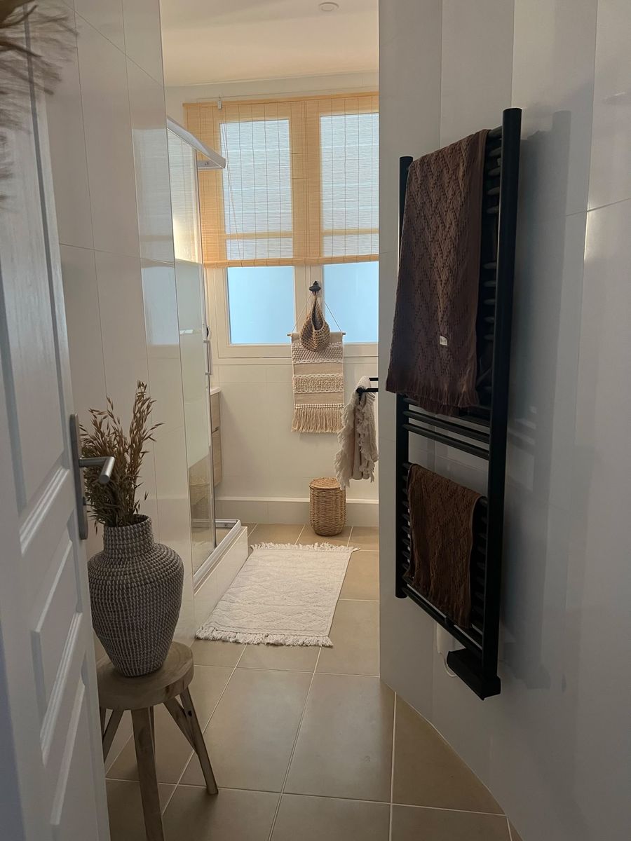 The bathroom after: a black towel radiator, a woven vase on a wooden stool and a bath mat