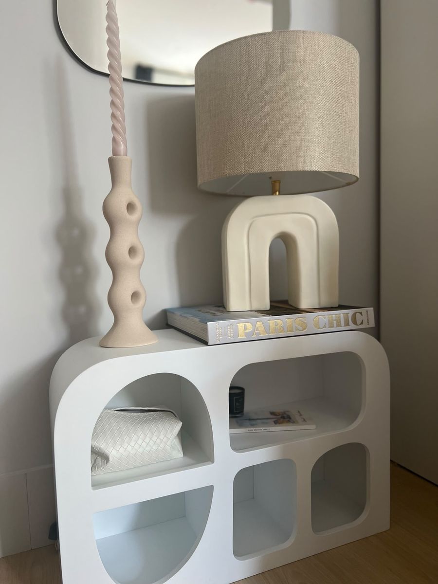 A sculptural white sideboard with an arched ceramic lamp and a twisted candle