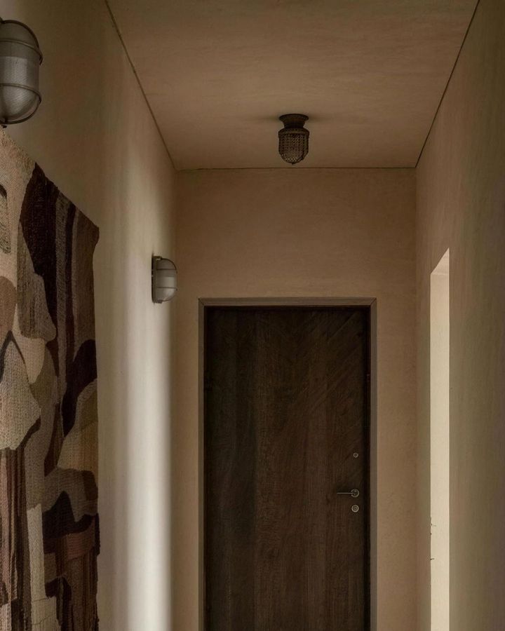 Limewashed hallway walls in the Meydan apartment, with a dark wood front door at the end