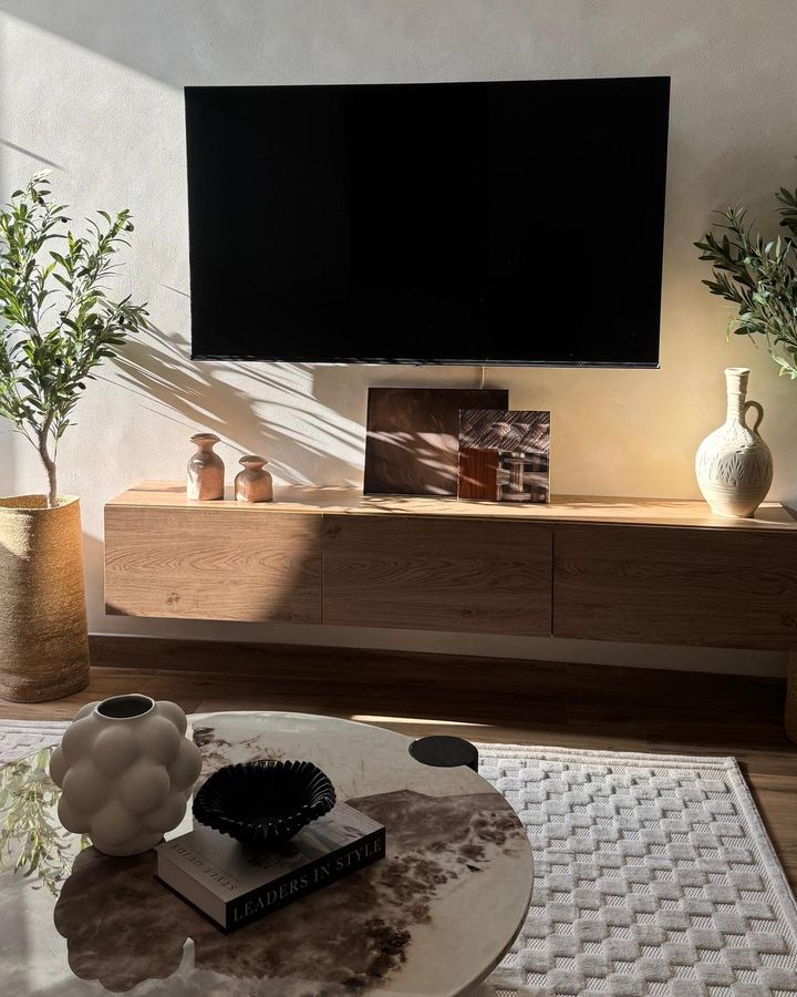 A floating oak console under the TV in the JVC apartment, with clay vases, framed prints and olive trees in late sun